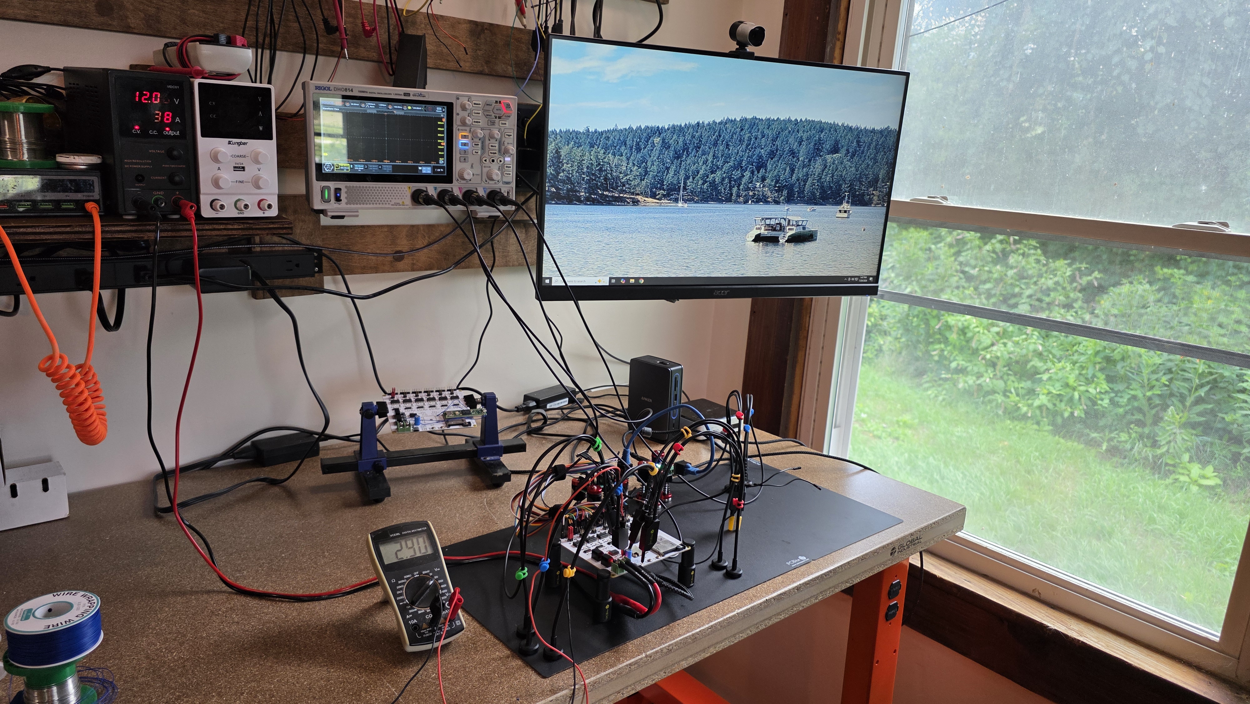 Photo of a test rig on my workbench. The CAN Gateway PCB is being probed by hands-free probes connected to an oscilloscope and a multimeter. A bench power supply is providing power. All six CAN buses are combined to a single CANable, which is connected to a nearby computer. A monitor on the wall uses a photo of "Catalyst," RTRF's first vessel design as desktop wallpaper.